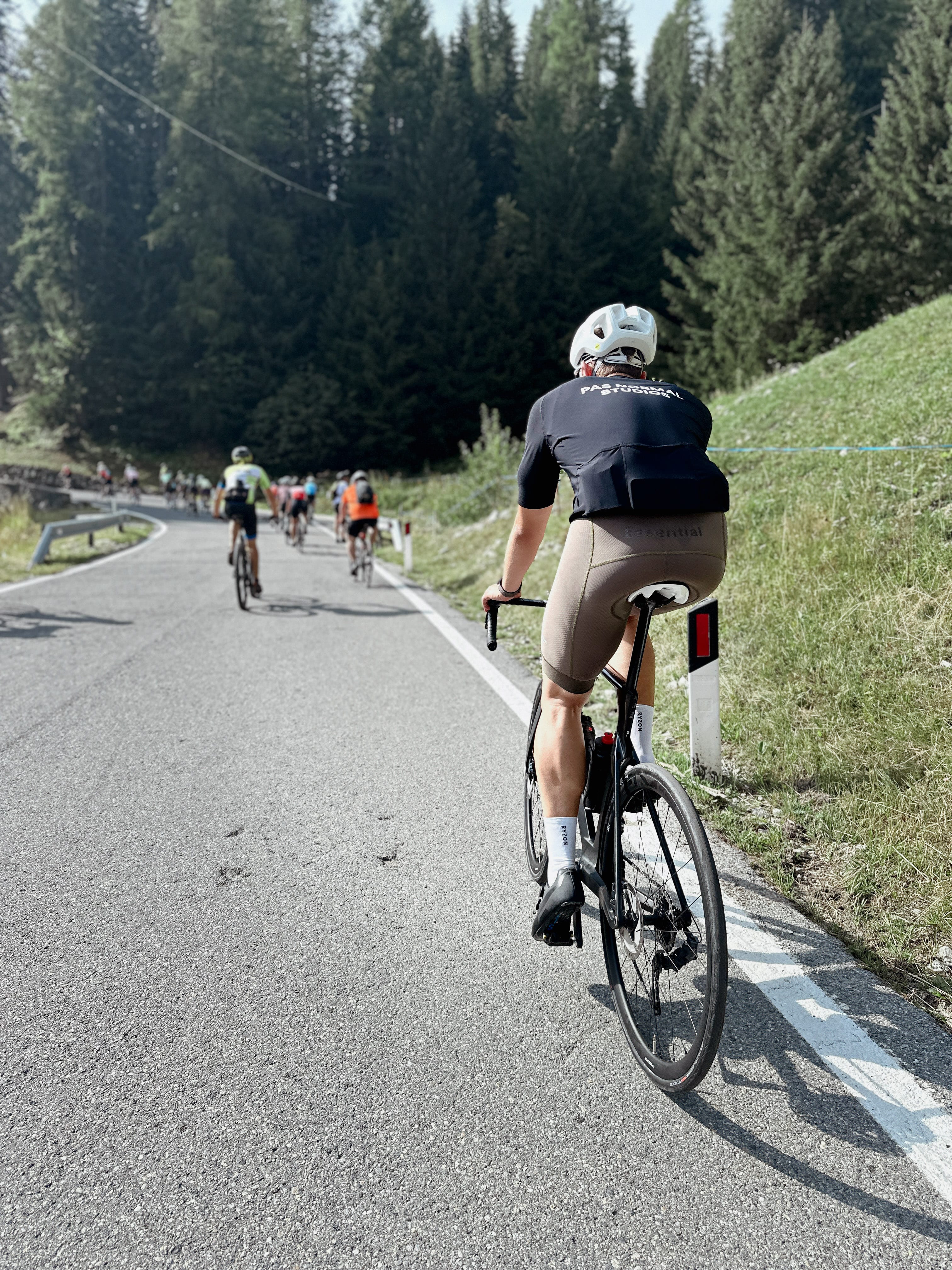 Ein Rennradfahrer fährt auf einer asphaltierten Bergstraße bergauf, vor ihm weitere Radfahrende im Hintergrund.
