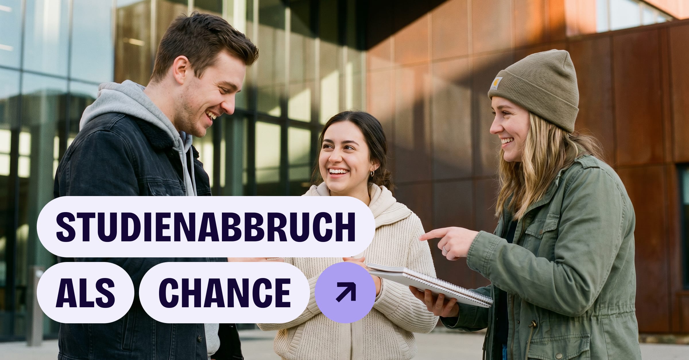 Drei junge Menschen unterhalten sich lächelnd vor einem modernen Gebäude, eine zeigt auf einen Collegeblock.